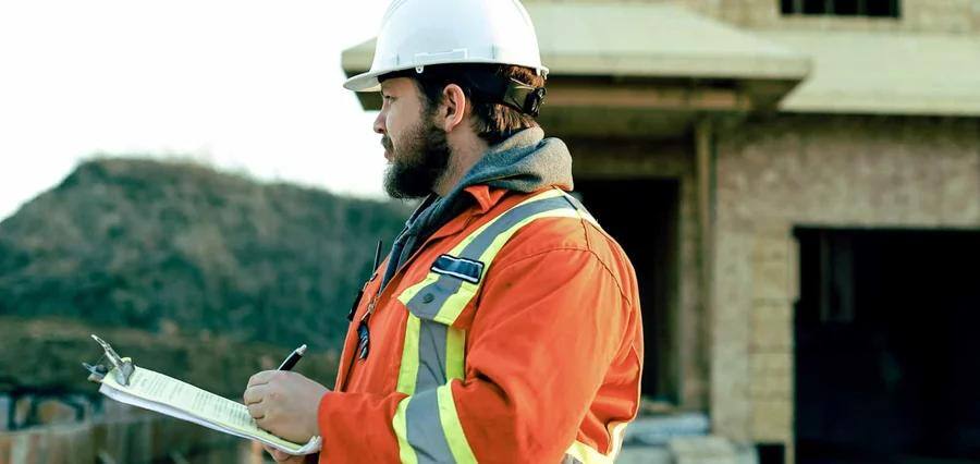 Man wearing construction gear and holding a pen and clip board.